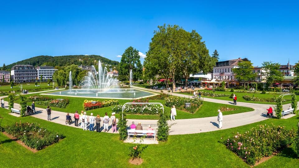 A park with a fountain, green lawns, and buildings in the background.