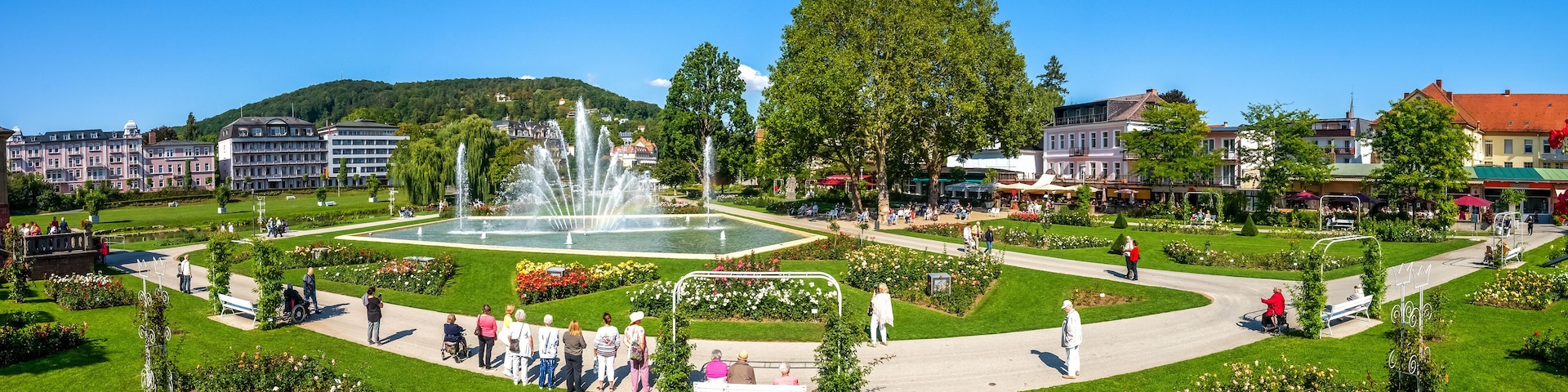 A park with a fountain, green lawns, and buildings in the background.
