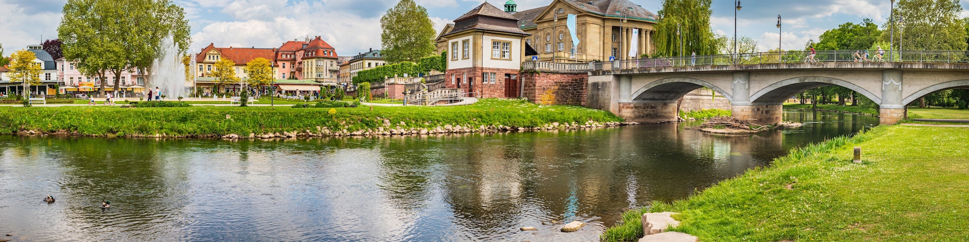 Un río con un puente de piedra, una fuente y edificios al fondo.