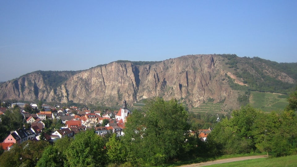 A town nestled at the base of a large cliff, with houses and a church visible.