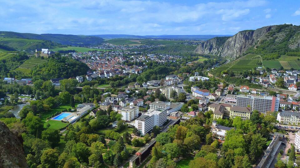 A town nestled in a valley with a castle on a hill, surrounded by lush greenery and mountains.