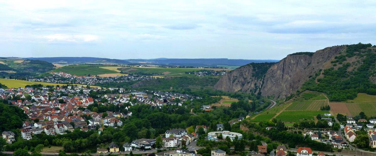 A town nestled in a valley with a prominent castle, surrounded by lush greenery and rolling hills.
