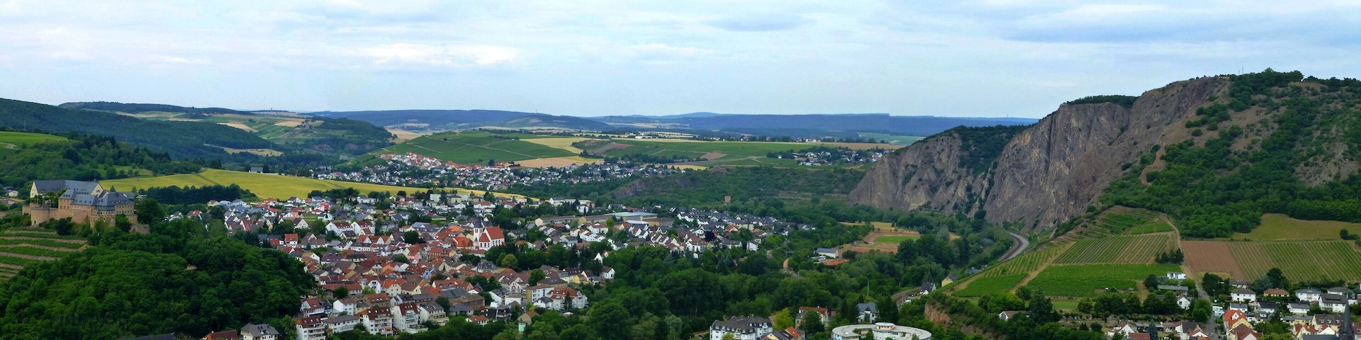A town nestled in a valley with a prominent castle, surrounded by lush greenery and rolling hills.