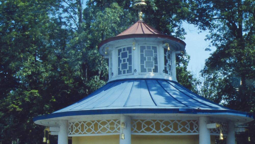 A gazebo with a blue roof and white columns, surrounded by trees.