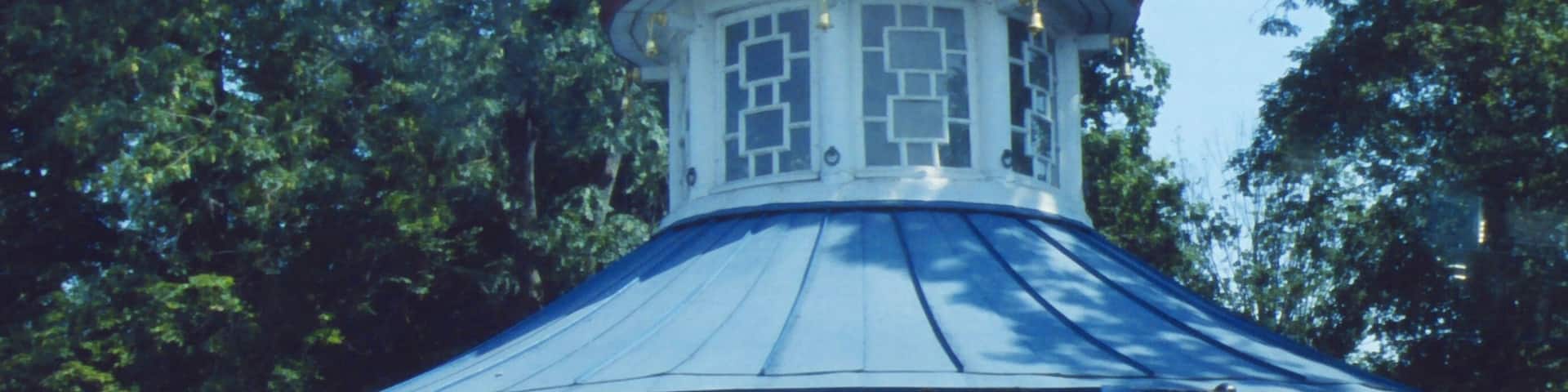 A gazebo with a blue roof and white columns, surrounded by trees.