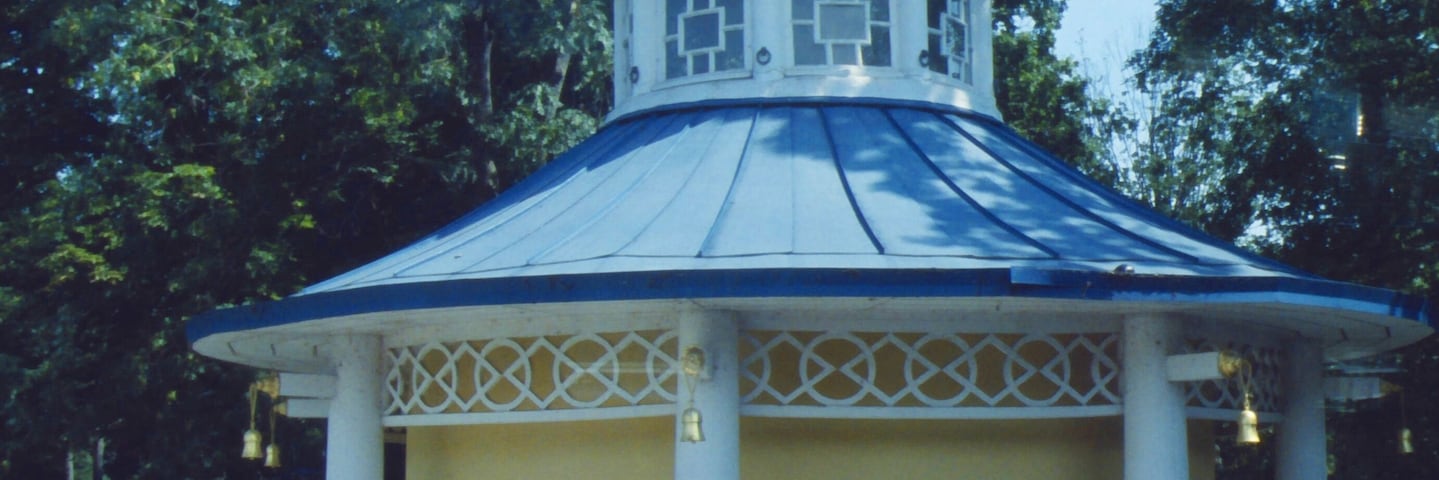 A gazebo with a blue roof and white columns, surrounded by trees.