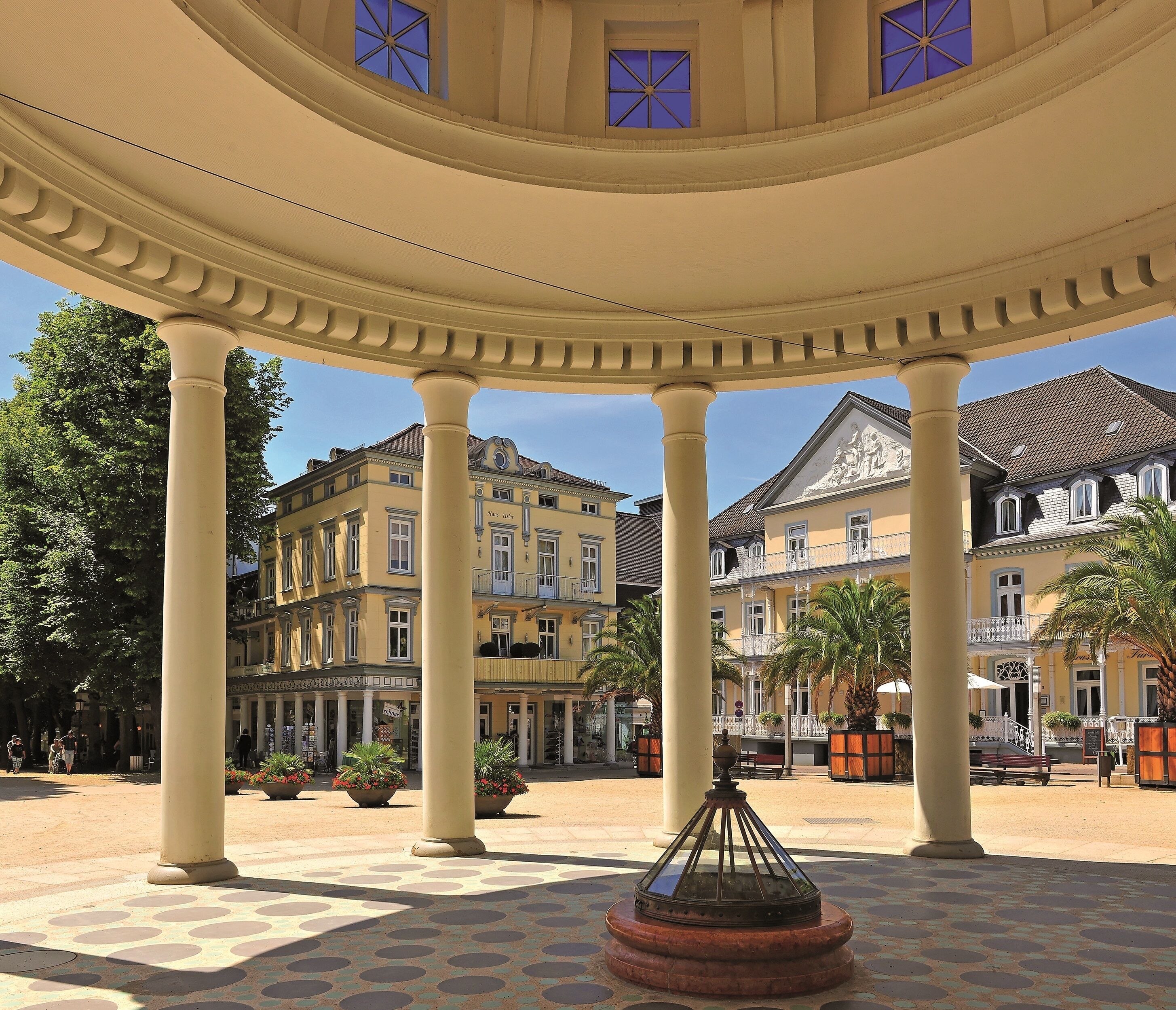 A covered courtyard with columns, a central fountain, and surrounding buildings with balconies and plants.