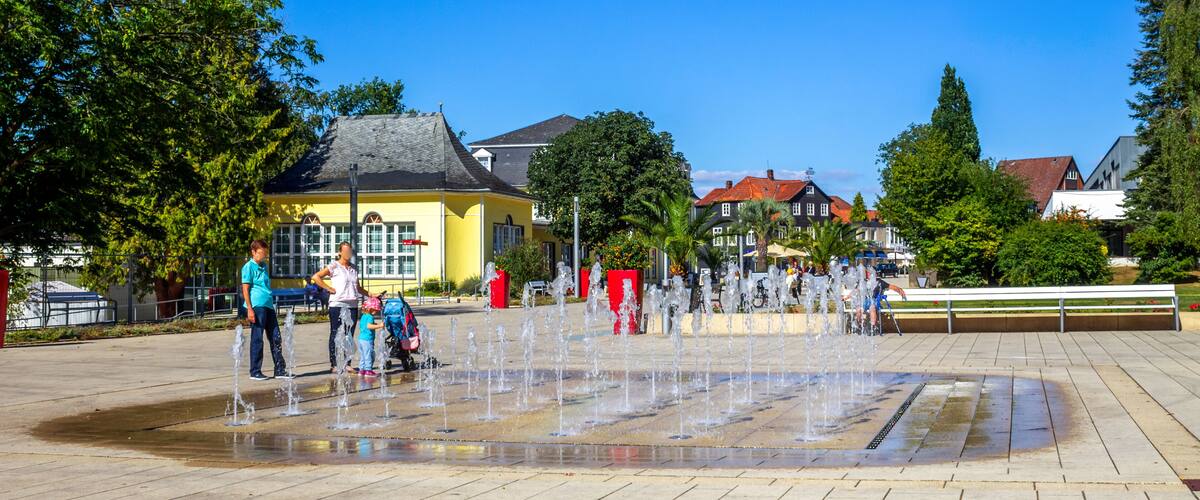 A public square with a water fountain, people, and surrounding buildings.