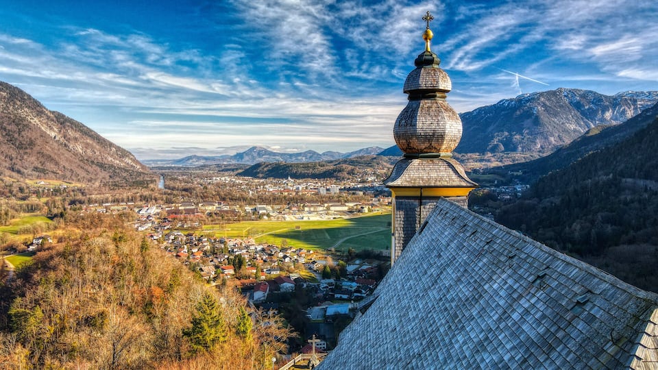 A church with a distinctive onion dome, a town in the valley below, and mountains in the background.