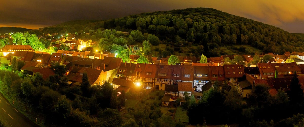 A village at night with illuminated houses and a forested hill in the background.