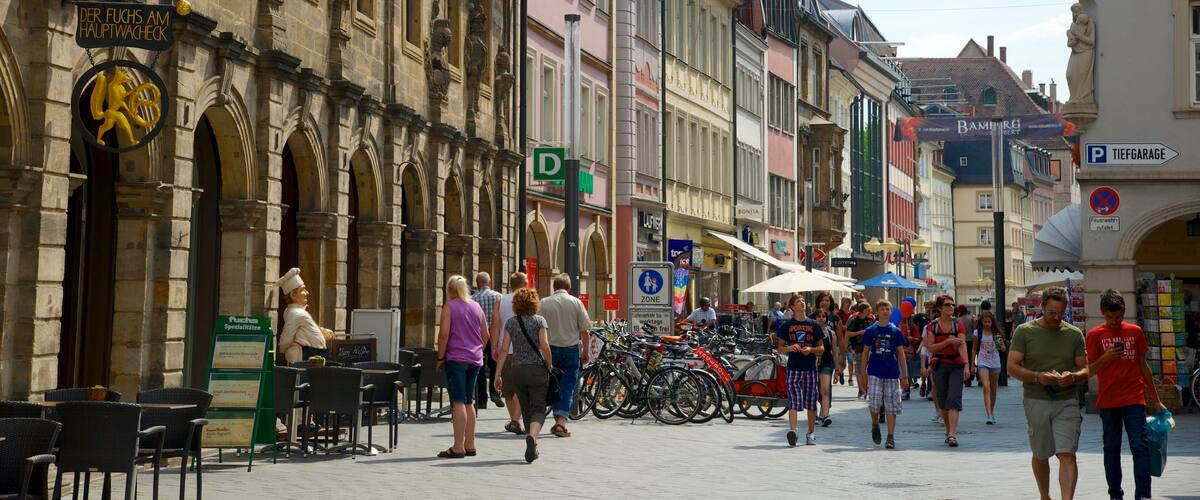 A historic European street with pedestrians, outdoor cafes, and bicycles.
