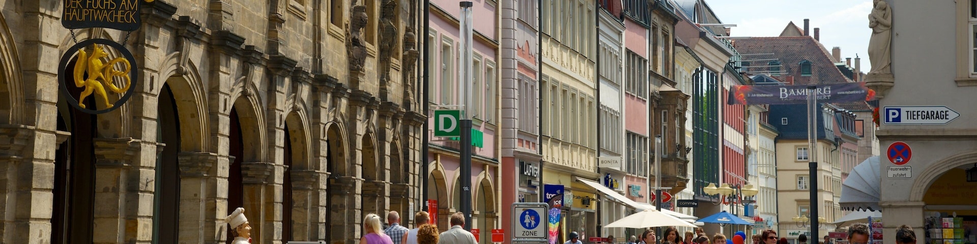 A historic European street with pedestrians, outdoor cafes, and bicycles.