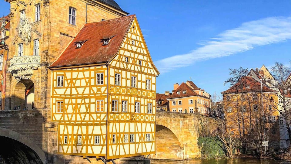 Un bâtiment à pans de bois surmonté d’un clocher, un pont de pierre et une rivière.
