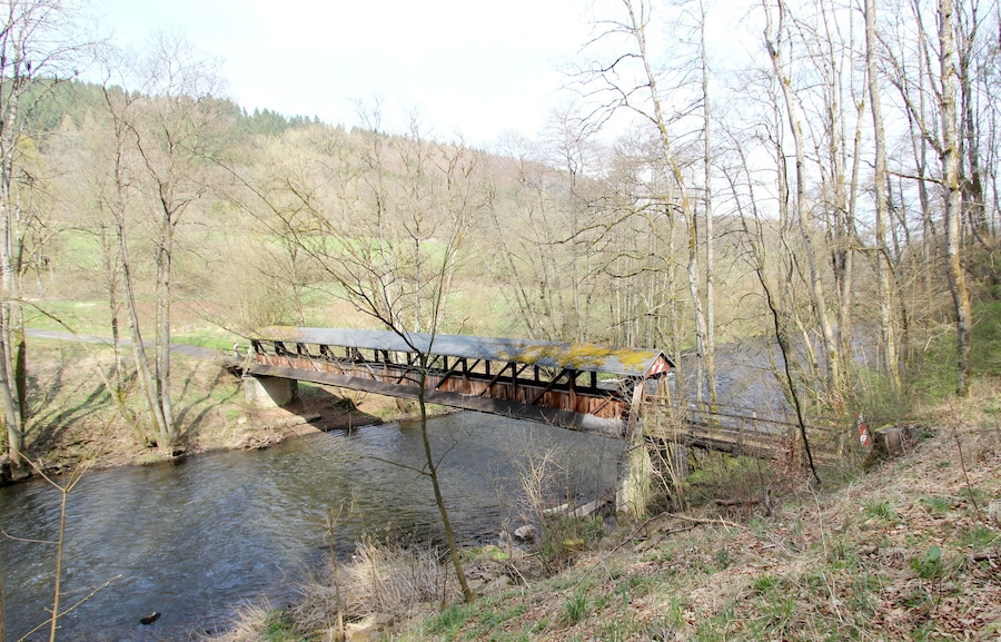 A wooden bridge over a river with trees and hills in the background.