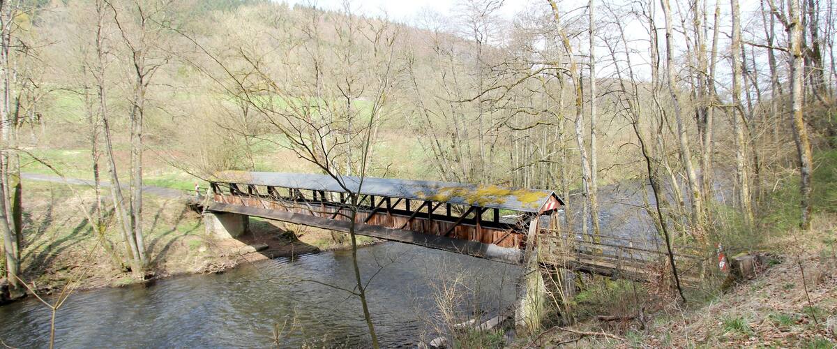 A wooden bridge over a river with trees and hills in the background.