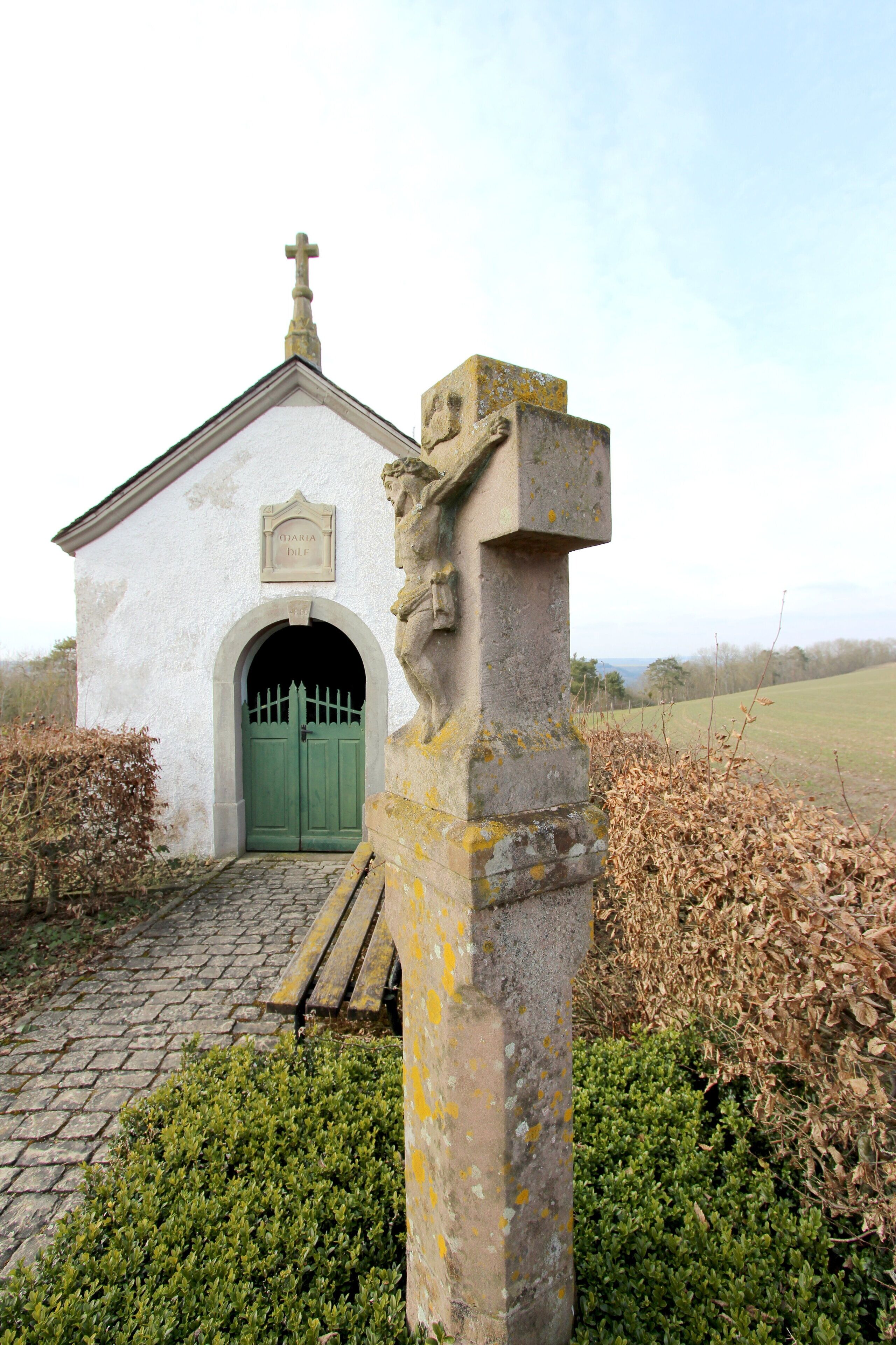 A small white church with a green door and a stone cross in front.