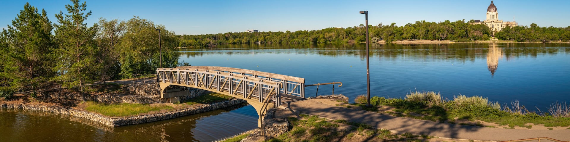 Tranquil Wascana Lake and the bridge along the walking trail of the lake park in Regina, Saskatchewan, Canada, with a view of the Saskatchewan Legislative Building.