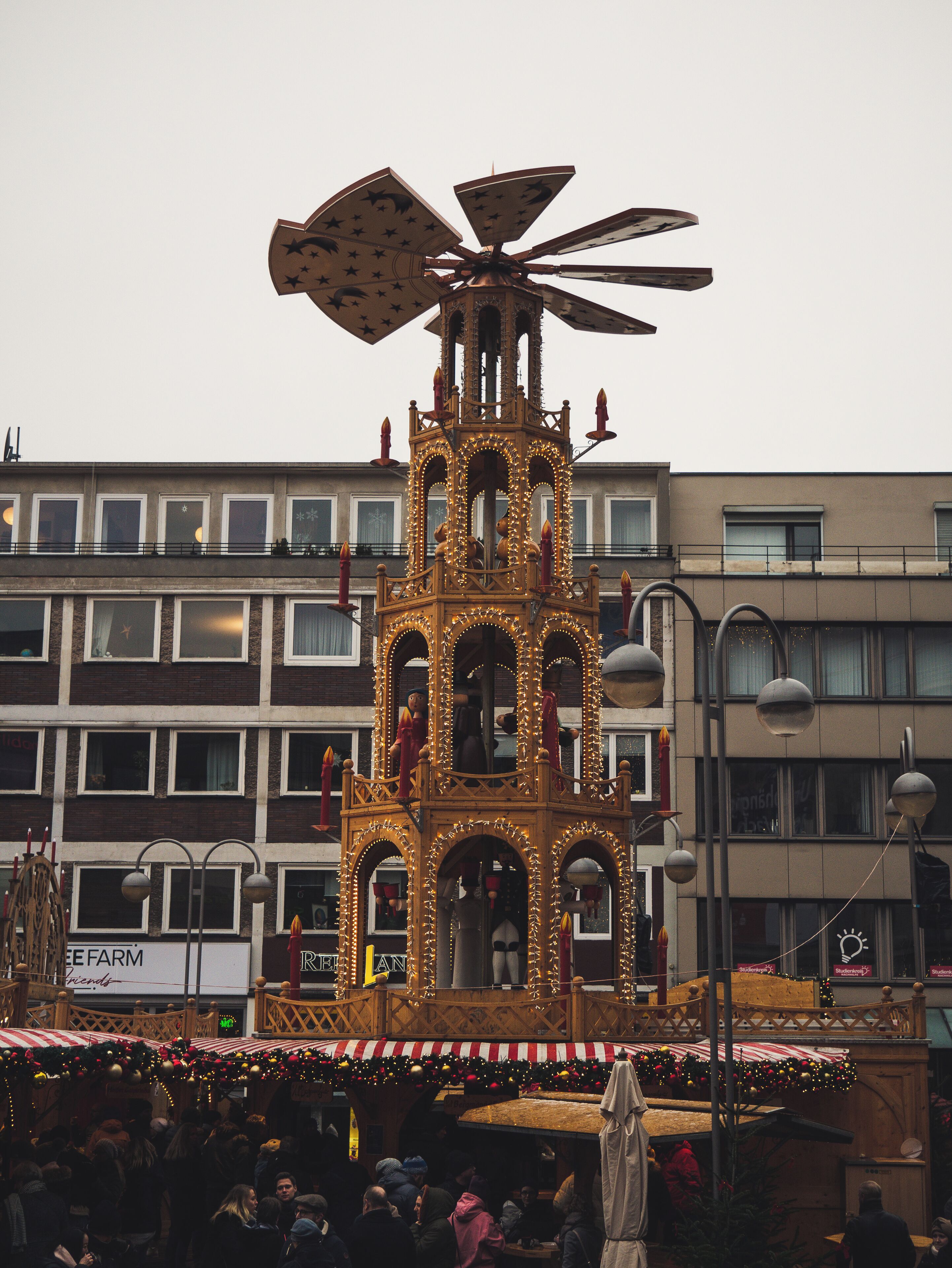 A decorated tower with a clock and a star-shaped top, surrounded by a crowd and buildings in the background.
