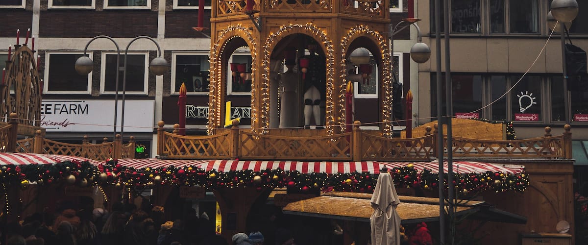A decorated tower with a clock and a star-shaped top, surrounded by a crowd and buildings in the background.