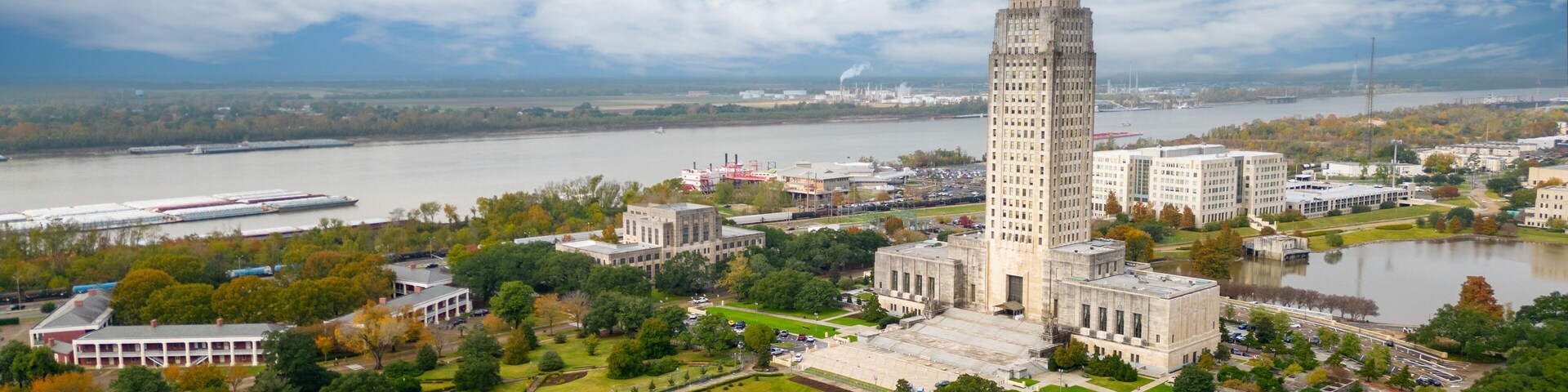 A large, historic building with a tall spire, surrounded by a well-maintained park and a river.
