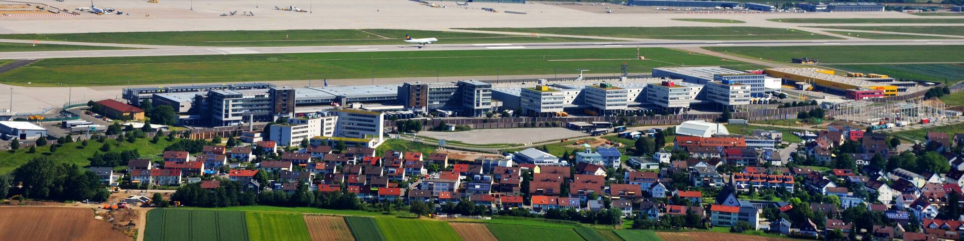 An aerial view of a town with a large airport, residential areas, and surrounding green fields.