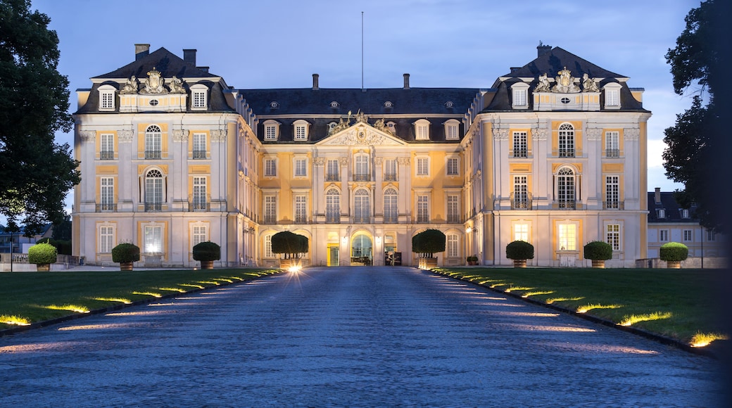 Ein prachtvolles, beleuchtetes Gebäude mit symmetrischer Architektur, einem Kopfsteinpflasterweg, der zum Eingang führt, und gepflegten Rasenflächen.