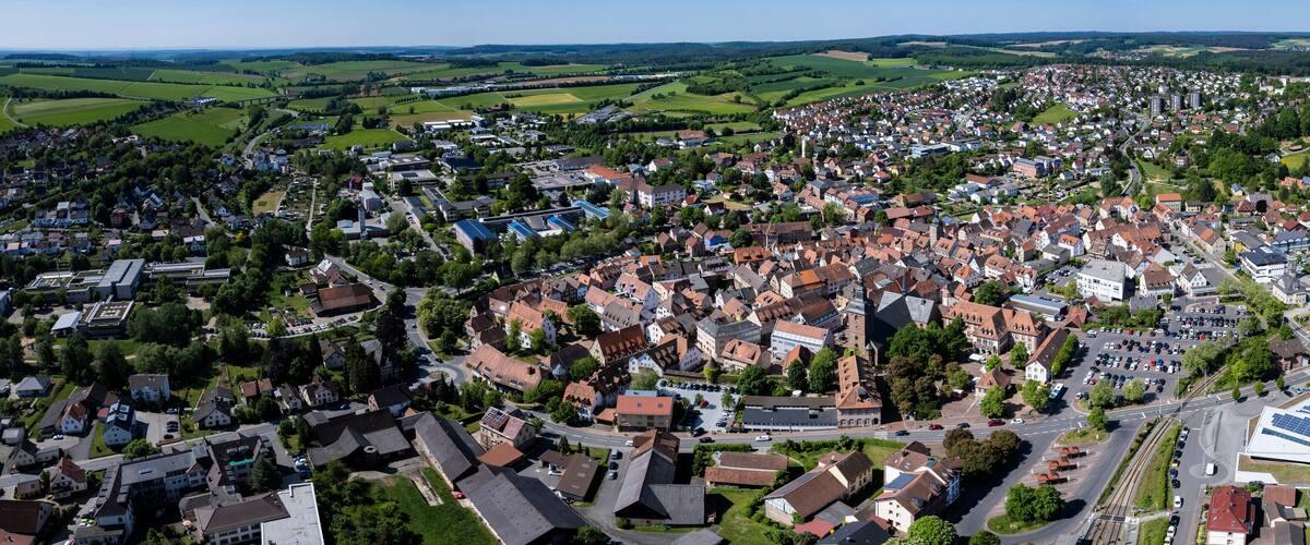 An aerial view of a town with a mix of residential houses, a central square, and surrounding green fields.