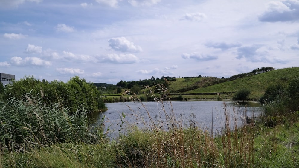 Un lac entouré de verdure et de collines, avec une grande structure industrielle sur la gauche.
