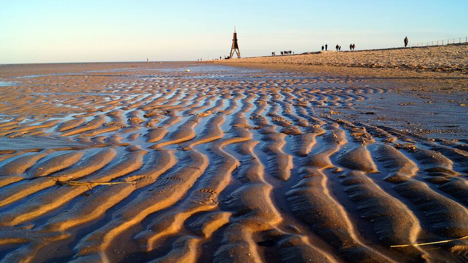 A beach with rippled sand patterns and a lighthouse in the distance.