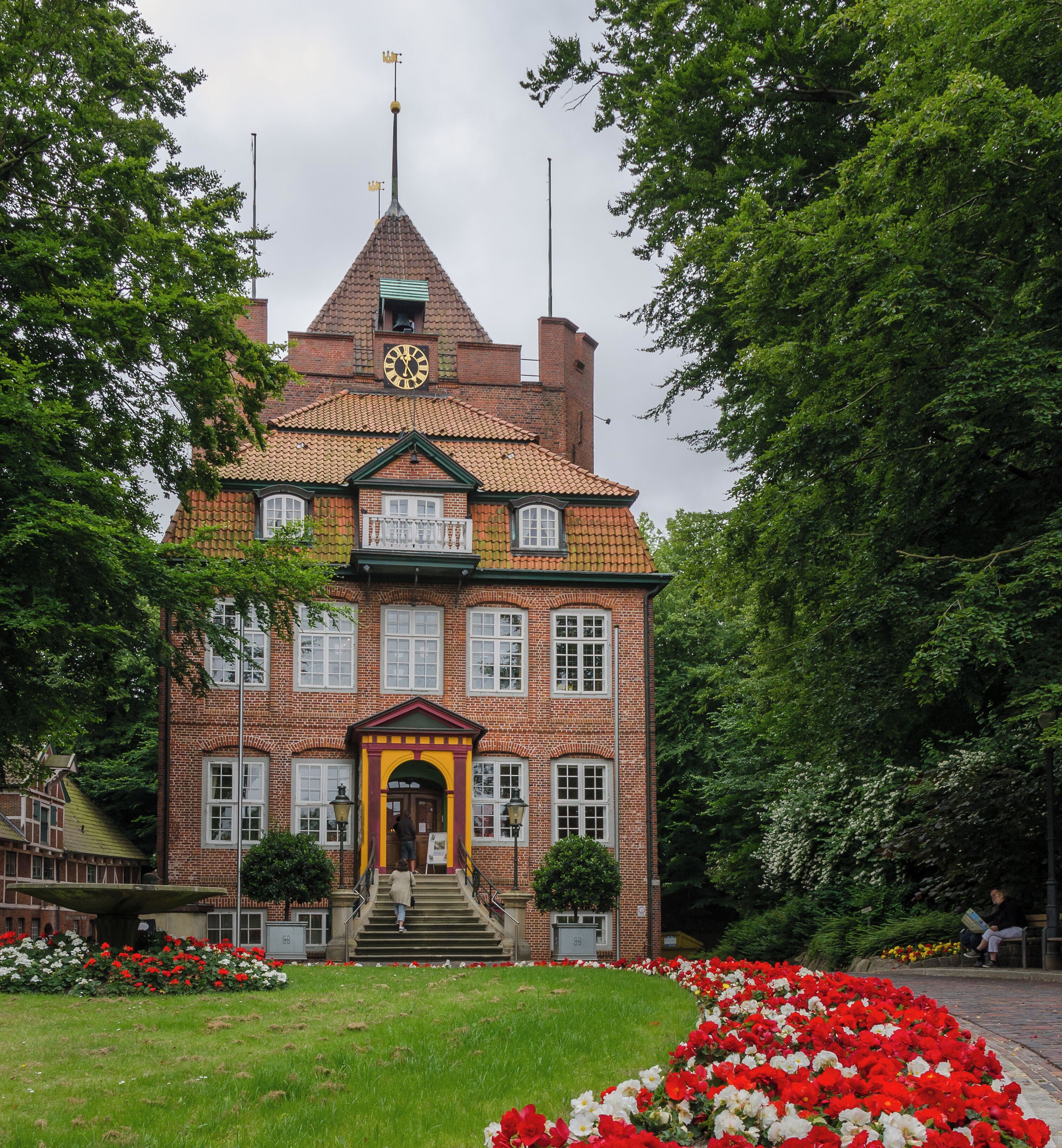 A historic building with a clock tower, surrounded by lush greenery and a vibrant flower garden.