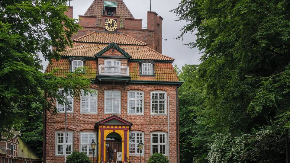 A historic building with a clock tower, surrounded by lush greenery and a vibrant flower garden.