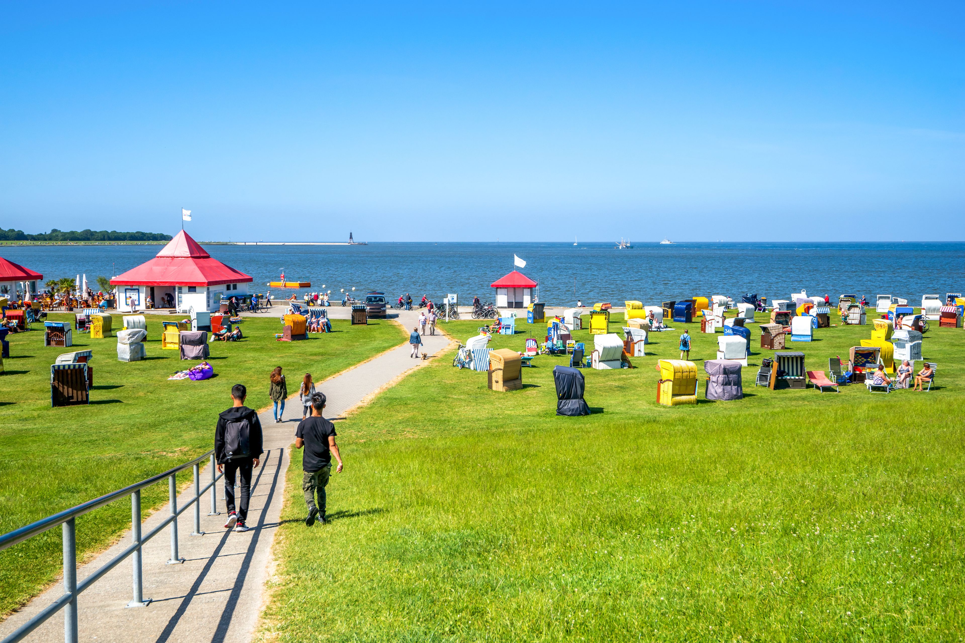 Eine Küstenlandschaft mit einer begrünten Promenade, bunten Strandhäusern und freiem Blick auf das Meer.