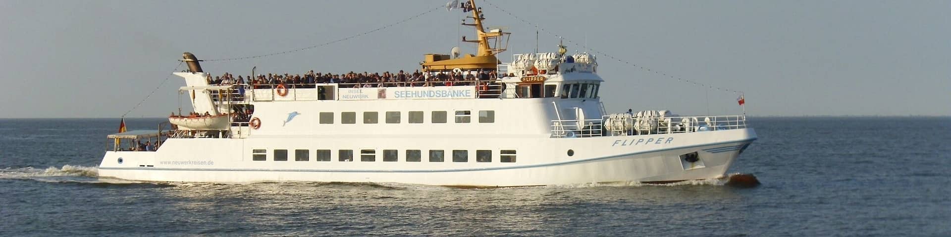 A white cruise ship named 'SEEHUNDSBÄNKE' with 'FLIPPER' written on the side, sailing on the water.