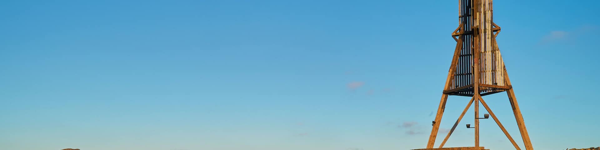 the historic beacon "Kugelbake" in Cuxhaven (Germany) seen in frog perspective from the mud flats of the Wadden Sea next to the groyne in beautiful late afternoon sunlight against blue sky