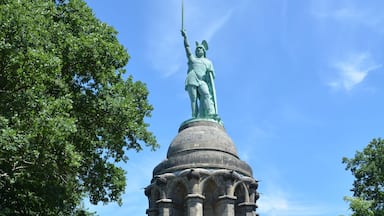Una estatua sobre un pedestal, con escalones que la llevan y rodeada de árboles.