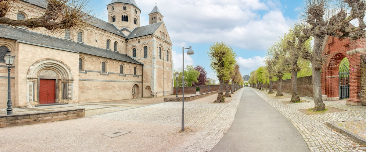 A cobblestone street lined with historic buildings, including a church with a prominent tower and a brick structure with a green archway.