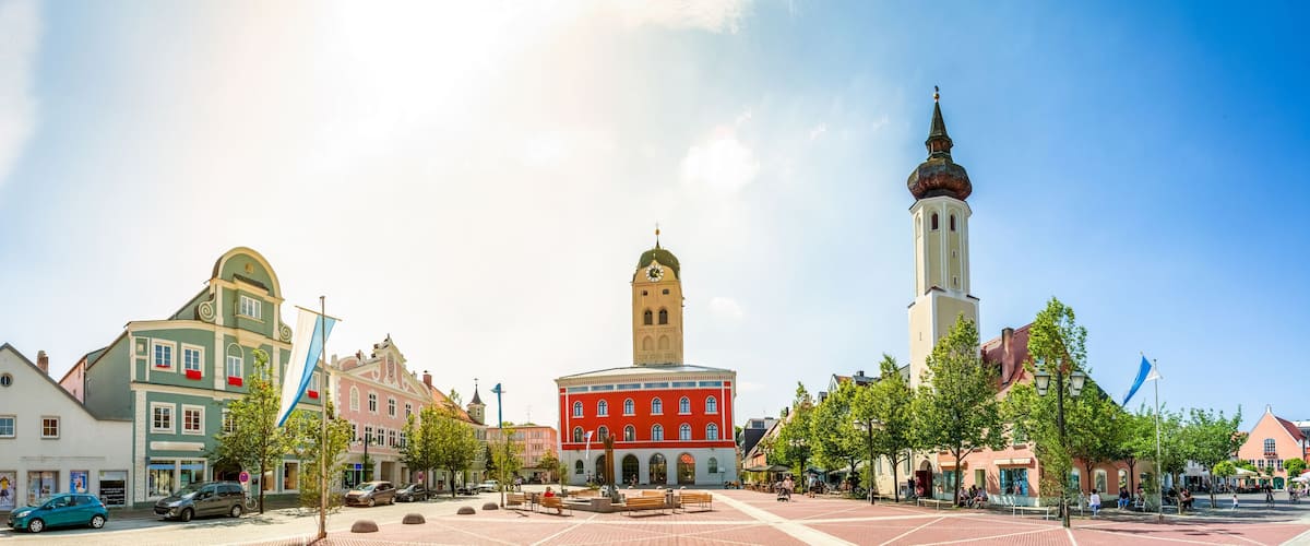A town square with historic buildings, a clock tower, and a church with a tall spire.