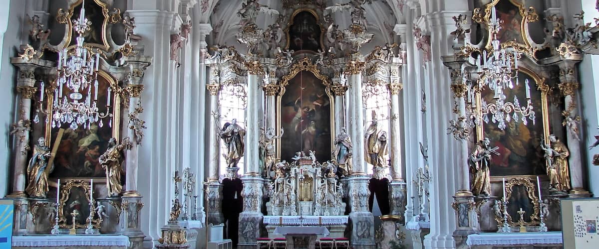 An ornate church interior with high ceilings, elaborate chandeliers, and religious statues.