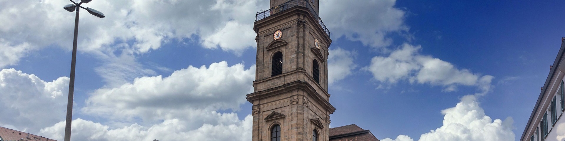 A historic building with a prominent clock tower, surrounded by other classic architecture and a clear blue sky with clouds.