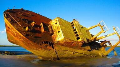 Un naufragio oxidado sobre una playa arenosa.