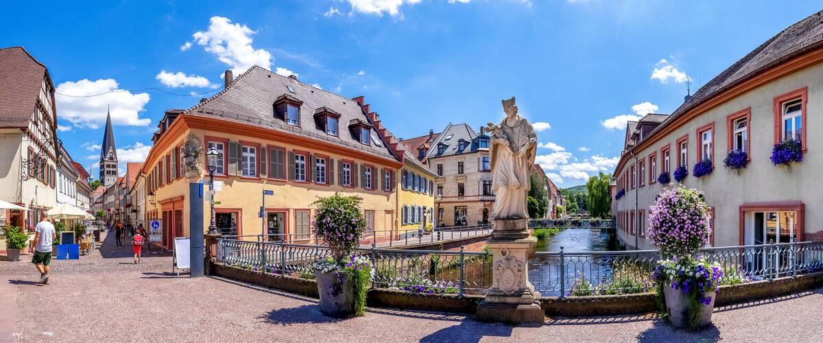 A cobblestone street with historic buildings, a statue, and a canal.