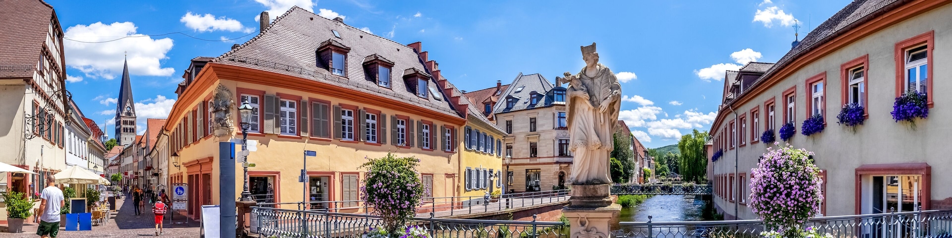 A cobblestone street with historic buildings, a statue, and a canal.