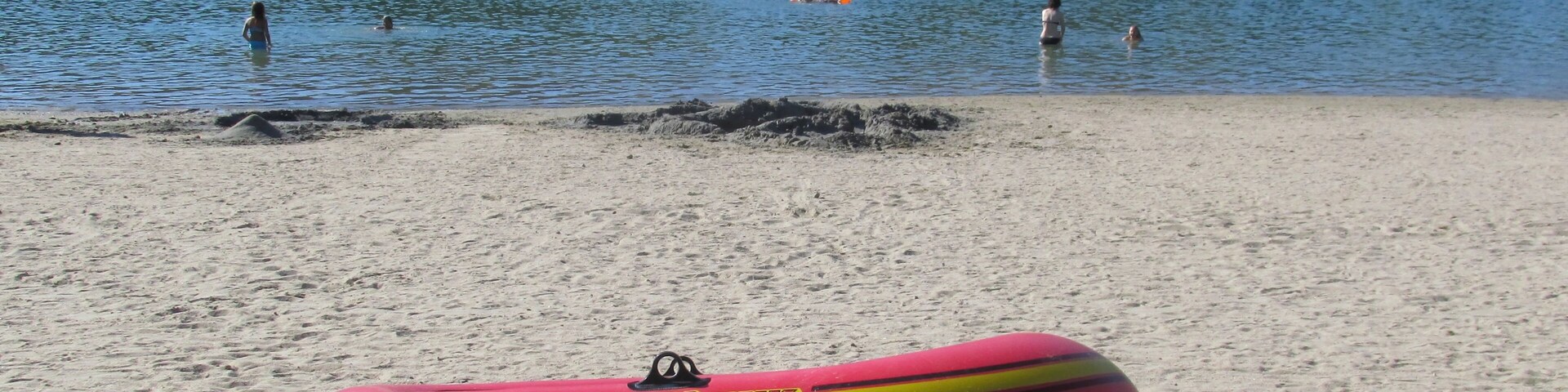 Una playa con un bote inflable rojo, dos remos y una pala sobre la arena.