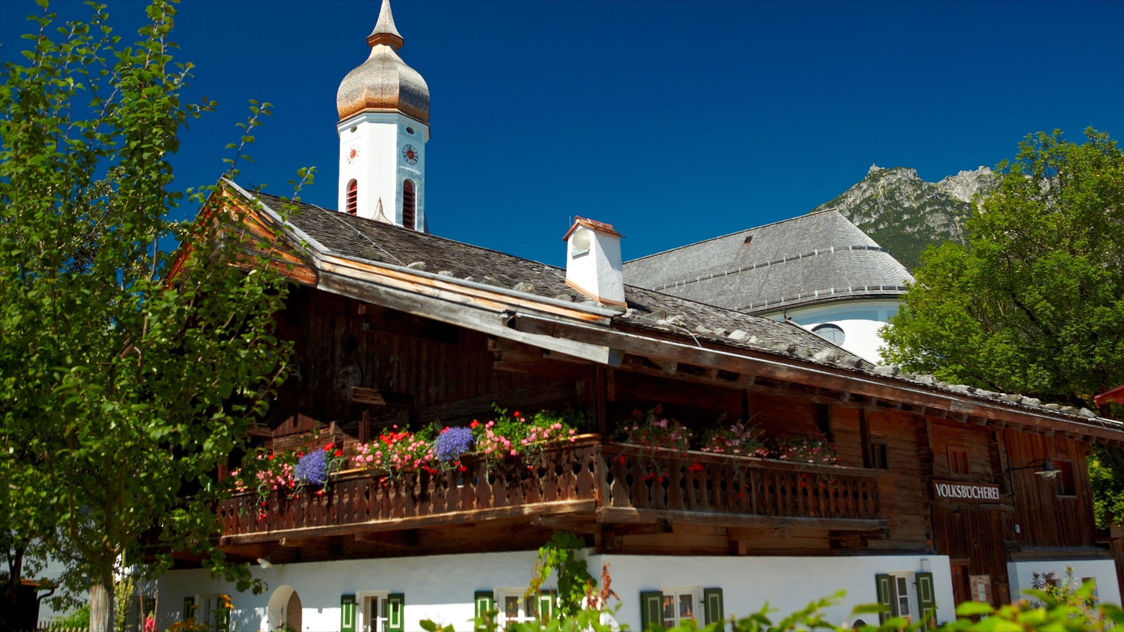 A traditional wooden building with a balcony, a church tower, and a mountain in the background.