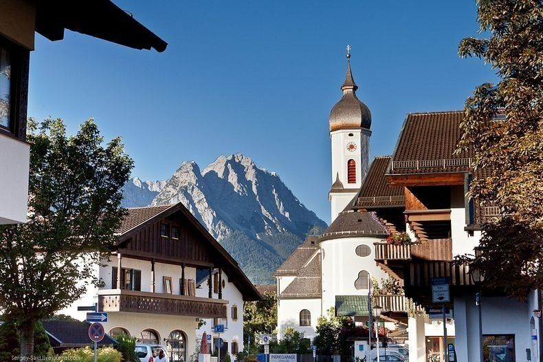 A mountain town with traditional buildings, a church, and a prominent mountain in the background.