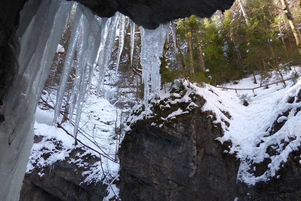Una grotta con stalattiti appese al soffitto e rocce coperte di neve.