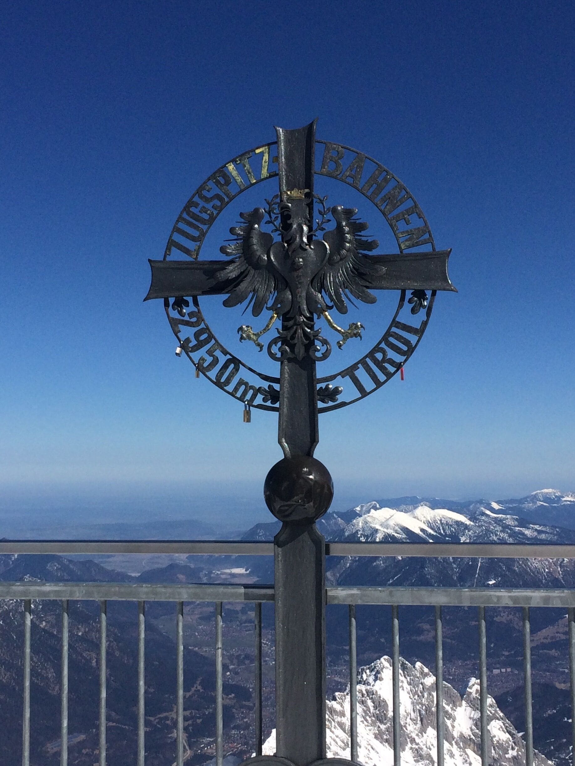 A cross with an eagle emblem and text, set against a mountainous backdrop.