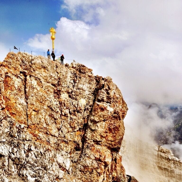 Une falaise rocheuse surmontée d’un monument doré, avec des personnes debout au sommet.