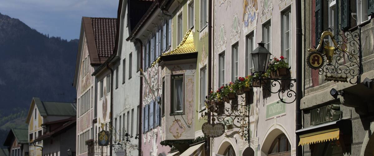 Una calle con arquitectura europea tradicional, que incluye fachadas ornamentadas y macetas con flores.