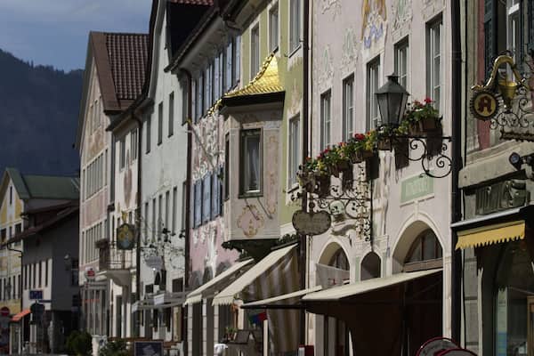Eine Straße mit traditioneller europäischer Architektur, darunter aufwendige Fassaden und Blumenkörbe.